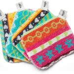 Four assorted color Skoy Scrubs, round with various patterns, arranged on a clean kitchen counter next to a sink.