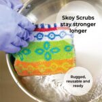 Four assorted color Skoy Scrubs, round with various patterns, arranged on a clean kitchen counter next to a sink.